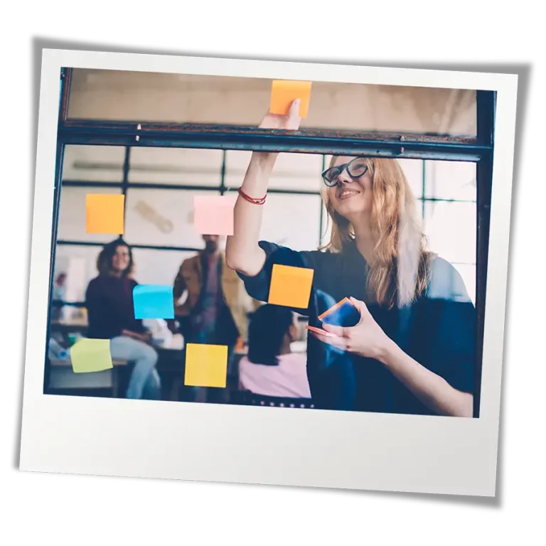 Leader in meeting placing post-it notes on window to facilitate collaboration between youth-serving organizations and teens.