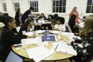 Youth sitting at circular tables talking with papers in front of them