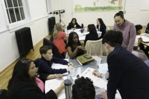 Youth at a circular table, one gentleman writing on a poster in the middle of the table